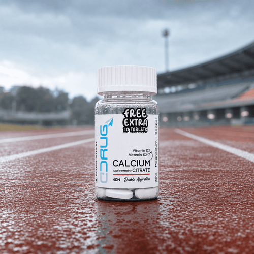 A bottle of Drug Rocket Free Extra 10 Tablets Calcium Carbonate Citrate standing on a wet red running track with a blurred stadium in the background. Running track shoot.
